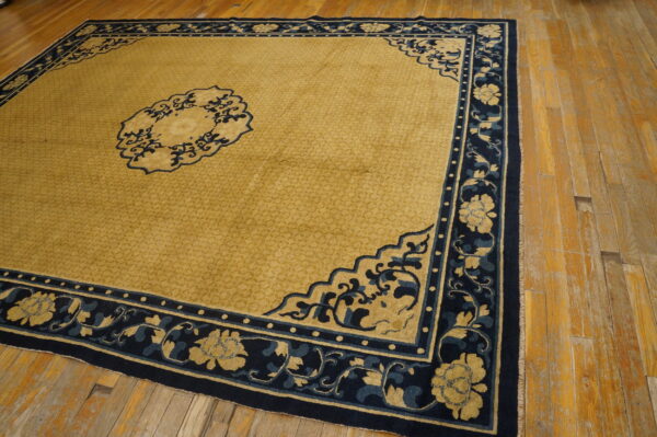 Low-pile gold rug featuring a navy blue floral border and medallion, displayed on aged wooden flooring.