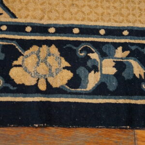 Close-up shows a navy, tan, and teal floral border rug resting on rustic wood planks.