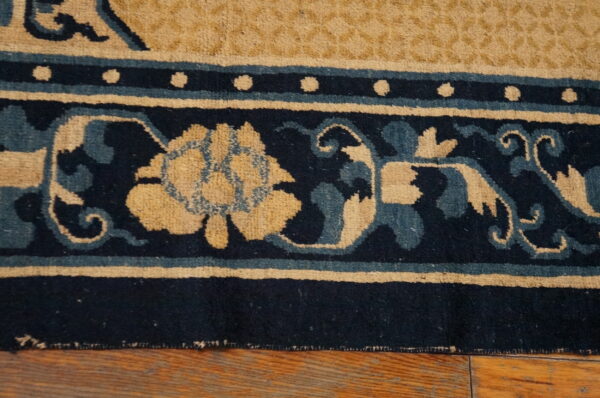Close-up shows a navy, tan, and teal floral border rug resting on rustic wood planks.