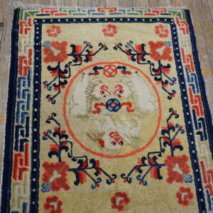 Cream rug with coral and navy designs, featuring a mythical creature medallion on worn wood flooring.