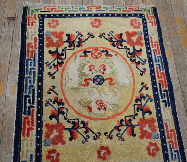 Cream rug with coral and navy designs, featuring a mythical creature medallion on worn wood flooring.