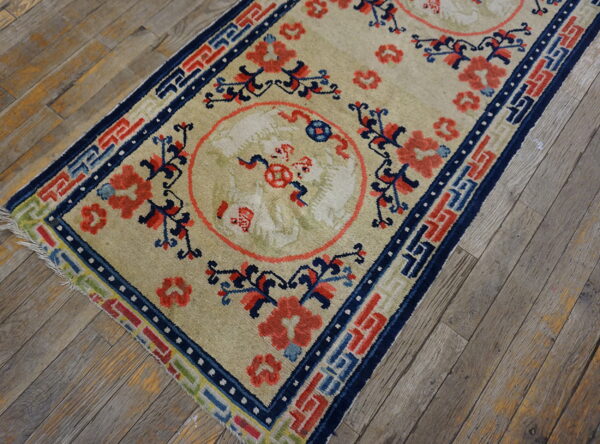 Beige rug runner with coral and navy blue medallions rests diagonally on weathered wood flooring.