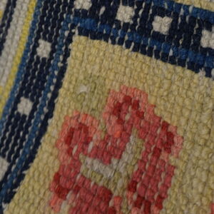 Textured close-up of a rug featuring geometric designs in coral, navy, cream, and yellow knots.