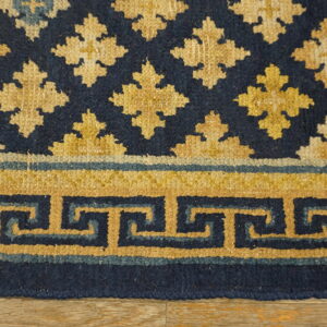 Detailed view of a navy and gold rug featuring a meander border and repeating floral motifs on wood floor.