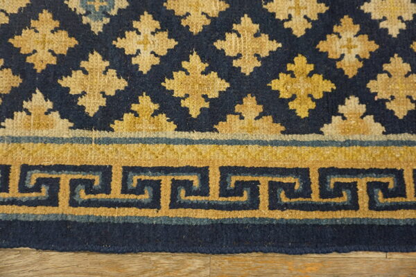 Detailed view of a navy and gold rug featuring a meander border and repeating floral motifs on wood floor.