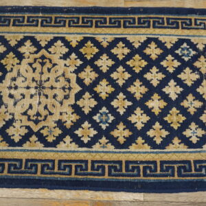 Low-pile navy and tan rug showing a geometric lattice field and Greek key border on wood flooring.