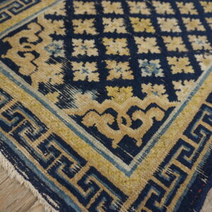 Navy blue and gold rug with detailed meander borders and floral patterns on rustic wood flooring.