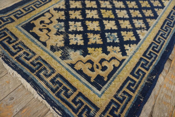Navy blue and gold rug with detailed meander borders and floral patterns on rustic wood flooring.
