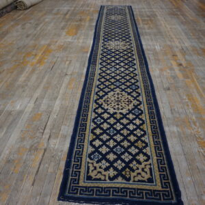 Navy and tan runner featuring geometric motifs and a key border on worn, multi-toned wood floors.