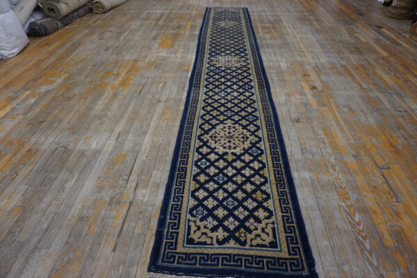 Navy and tan runner featuring geometric motifs and a key border on worn, multi-toned wood floors.