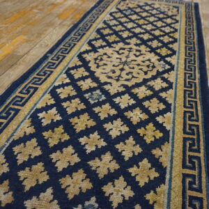Navy blue runner rug with gold Greek key border and repeating geometric floral patterns on wood flooring.