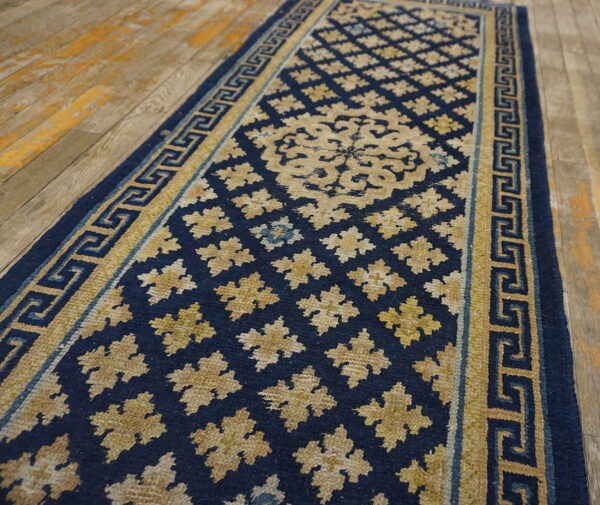 Navy blue runner rug with gold greek key border and repeating geometric floral patterns on wood flooring.
