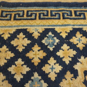 Textured navy blue, gold, and light blue rug featuring a Greek key border and quatrefoil medallions.