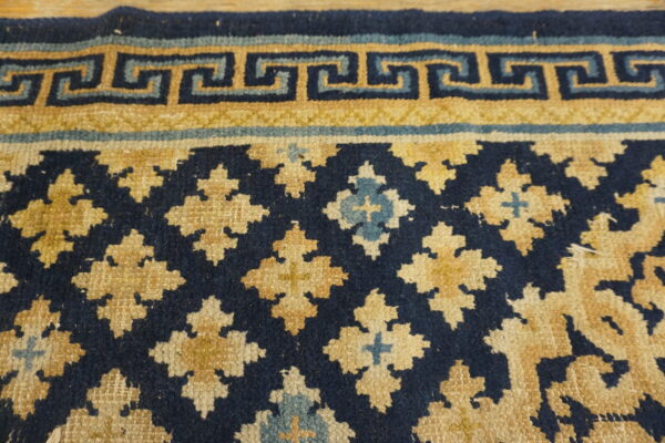 Textured navy blue, gold, and light blue rug featuring a greek key border and quatrefoil medallions.