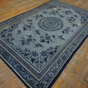 A slate blue area rug with dark navy floral patterns and a geometric border is centered on rustic wooden planks.