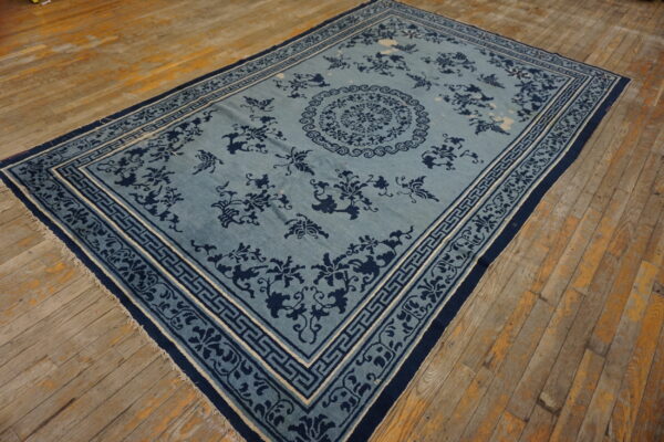 A slate blue area rug with dark navy floral patterns and a geometric border is centered on rustic wooden planks.