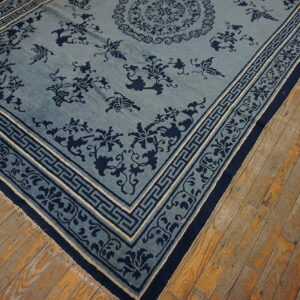 Light blue rug with deep blue floral and geometric patterns rests on distressed plank wood floors.