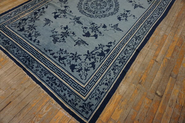 Light blue rug with deep blue floral and geometric patterns rests on distressed plank wood floors.