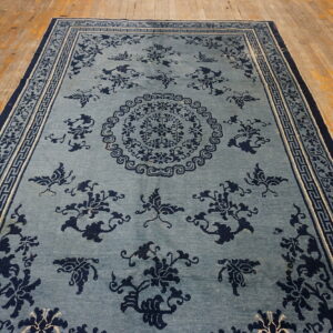 Light blue rug with navy floral and butterfly motifs, bordered by Greek key patterns, displayed on wood floors.