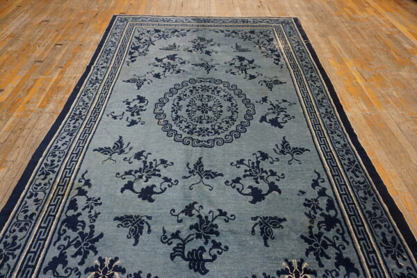 Light blue rug with navy floral and butterfly motifs, bordered by greek key patterns, displayed on wood floors.