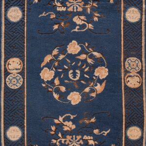 Detail of a blue rug with tan floral designs and a border featuring brown fretwork and circular medallions.