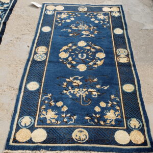 Blue runner rug with cream floral patterns and geometric borders displayed on textured concrete ground.