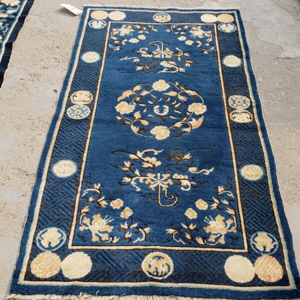 Blue runner rug with cream floral patterns and geometric borders displayed on textured concrete ground.