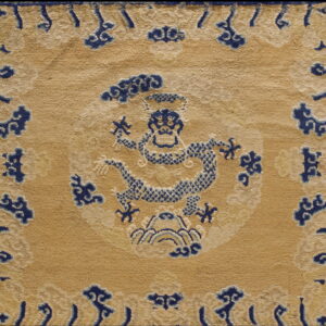 Muted gold rug with a detailed central navy blue dragon pattern and blue scrolling cloud border motifs.