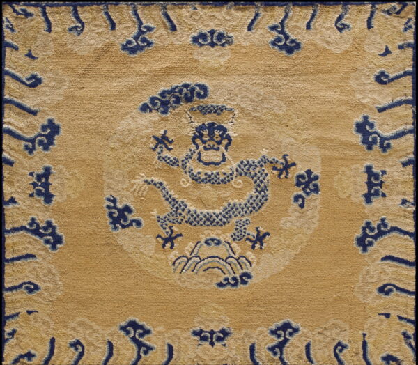 Muted gold rug with a detailed central navy blue dragon pattern and blue scrolling cloud border motifs.