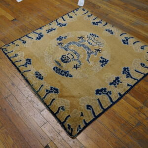 Low-pile golden rug with a navy blue dragon and cloud motif lying on distressed brown plank flooring.