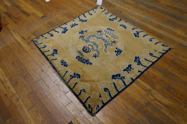Low-pile golden rug with a navy blue dragon and cloud motif lying on distressed brown plank flooring.