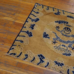 A gold and indigo blue dragon-pattern rug with low pile rests on distressed hardwood flooring.