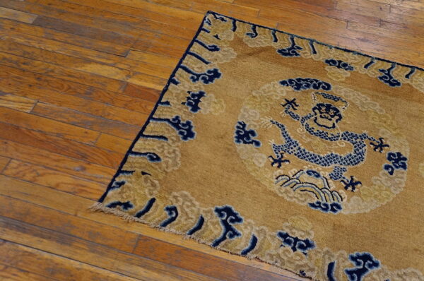 A gold and indigo blue dragon-pattern rug with low pile rests on distressed hardwood flooring.