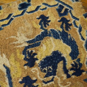 Distressed rug featuring deep blue and gold abstract designs on a tan background, shown on warm hardwood flooring.