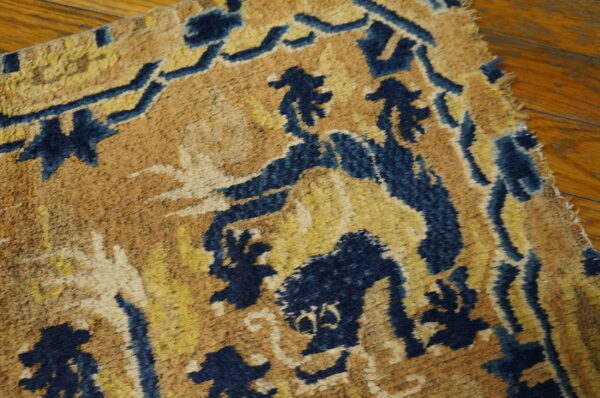 Distressed rug featuring deep blue and gold abstract designs on a tan background, shown on warm hardwood flooring.