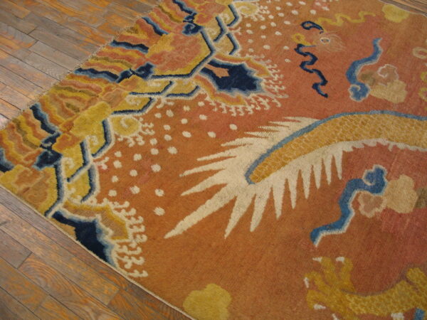 A colorful area rug with bold orange, yellow, and navy blue patterns sits on rustic wood flooring.