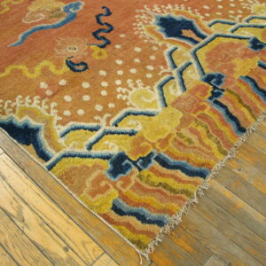 Diagonal view of a low pile orange rug featuring a stylized yellow and navy blue pattern on distressed wood.