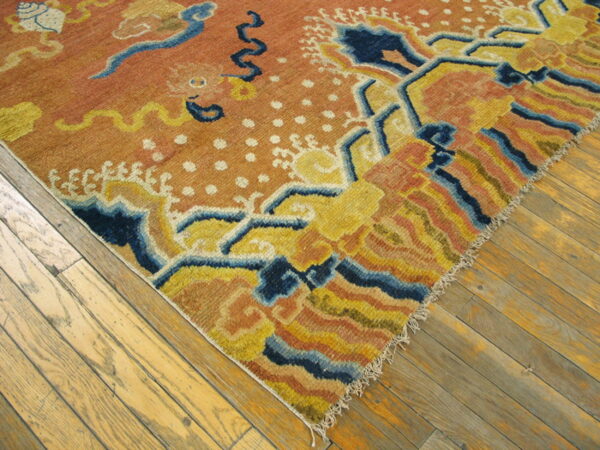 Diagonal view of a low pile orange rug featuring a stylized yellow and navy blue pattern on distressed wood.
