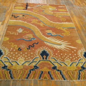 Yellow dragon and blue cloud motifs dominate this rust-colored rug resting on wooden floorboards.