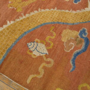 Rust and gold rug with blue accents features a seashell and cloud patterns resting on wood floorboards.