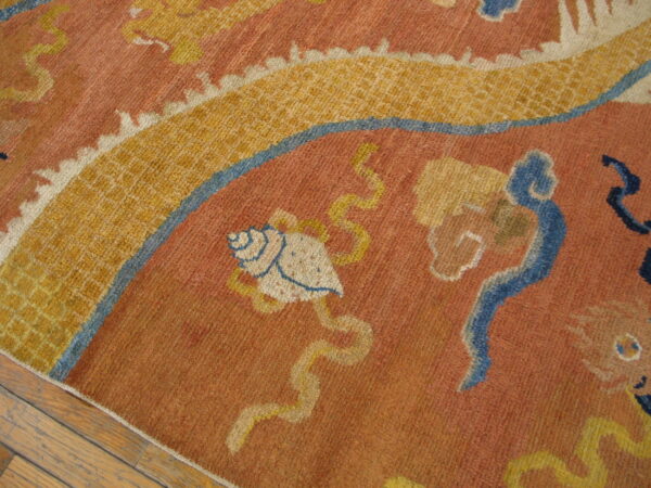Rust and gold rug with blue accents features a seashell and cloud patterns resting on wood floorboards.