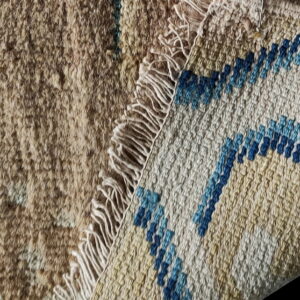 A beige shaggy rug face is turned back to show the cream and blue geometric woven backing.
