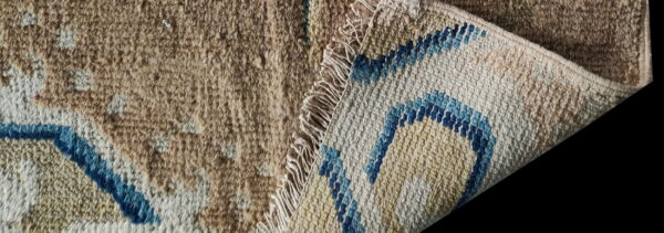 A beige shaggy rug face is turned back to show the cream and blue geometric woven backing.