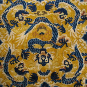 Intricate yellow rug detail with dense, dark blue and ivory zoomorphic patterned motifs.