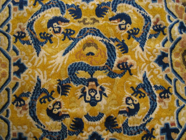 Intricate yellow rug detail with dense, dark blue and ivory zoomorphic patterned motifs.