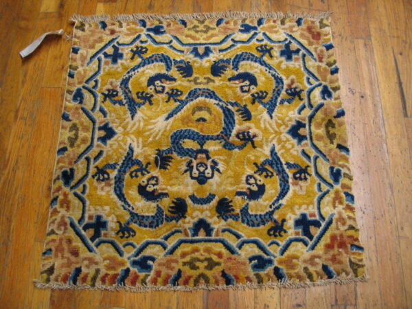 High-pile square rug with blue dragon figures on a golden field, resting on light wood flooring.