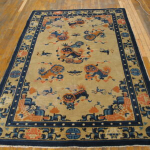 Ornate tan rug featuring blue and orange mythological animal patterns with a dark navy blue geometric border on wood flooring.