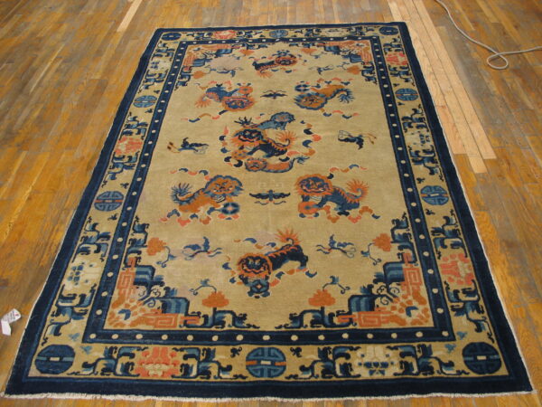 Ornate tan rug featuring blue and orange mythological animal patterns with a dark navy blue geometric border on wood flooring.