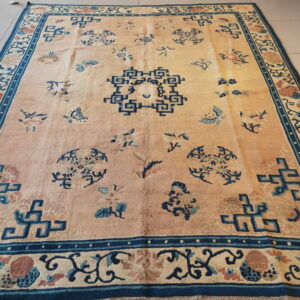 Pale peach rug with scattered dark blue geometric and floral motifs and a wide patterned border on tile.