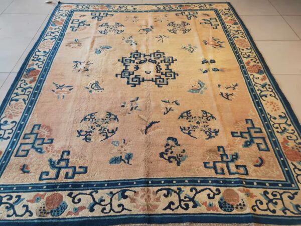 Pale peach rug with scattered dark blue geometric and floral motifs and a wide patterned border on tile.